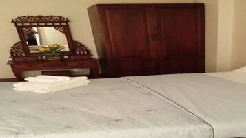Una cama bien hecha con una colcha de motivos florales, un aparador de madera con un espejo y un jarrón de flores, y un armario grande.