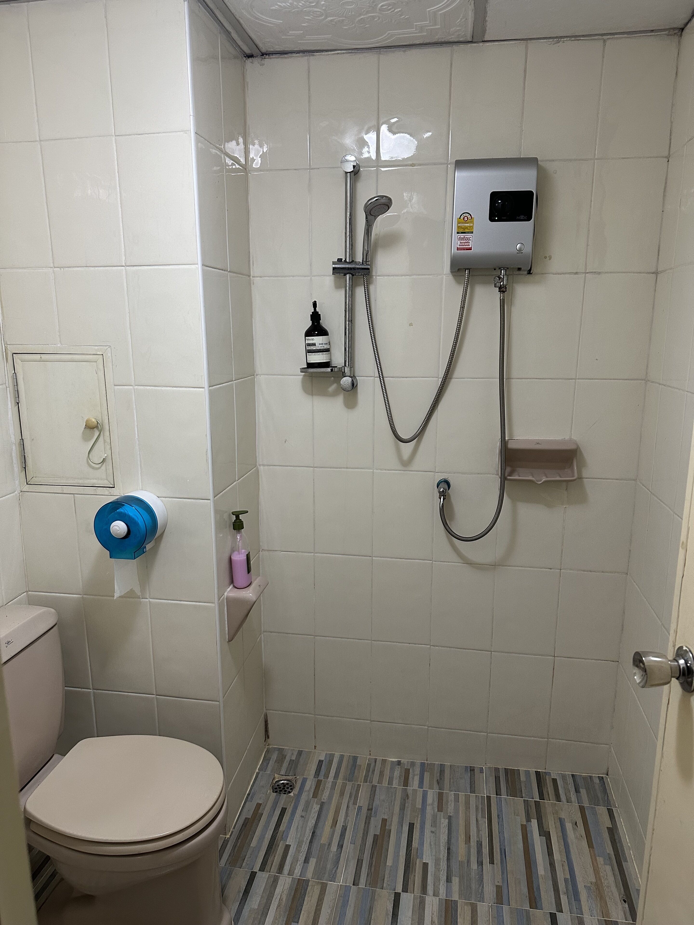 Ein kleines Badezimmer mit Fliesen, einer Toilette, einer Dusche und einem Seifenspender.