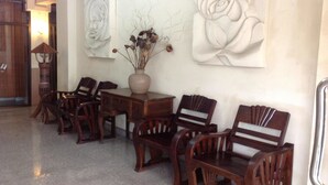 Una habitación con sillas de madera y una mesa, un jarrón con flores secas, y dos grandes obras de arte en la pared.