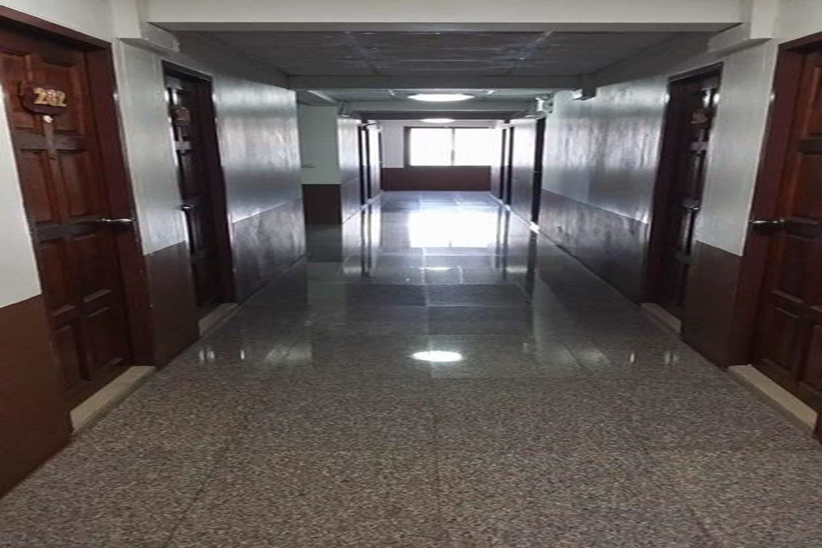 A long, narrow hallway with polished granite floors and wooden doors on both sides.