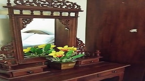 Una cómoda de madera con espejo, cajones y un florero con flores amarillas.