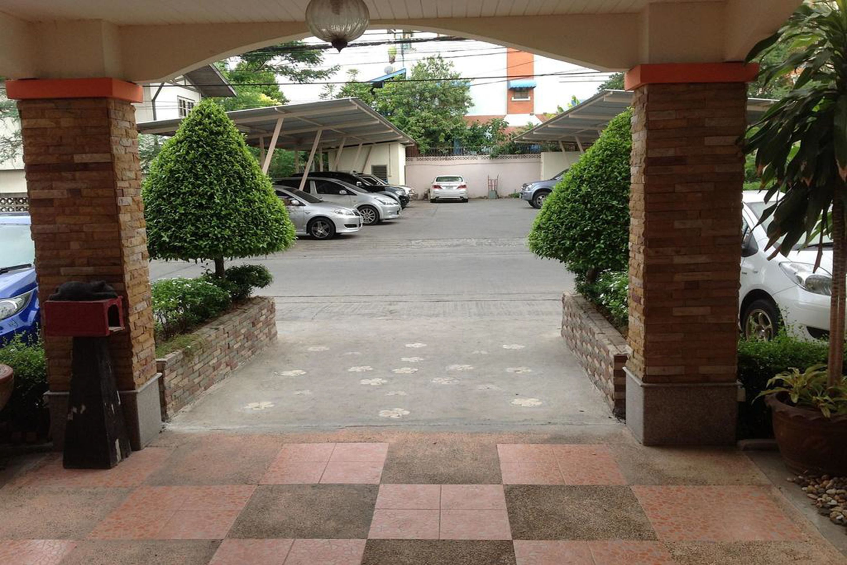 A covered parking area with cars, a tiled walkway, and potted plants.