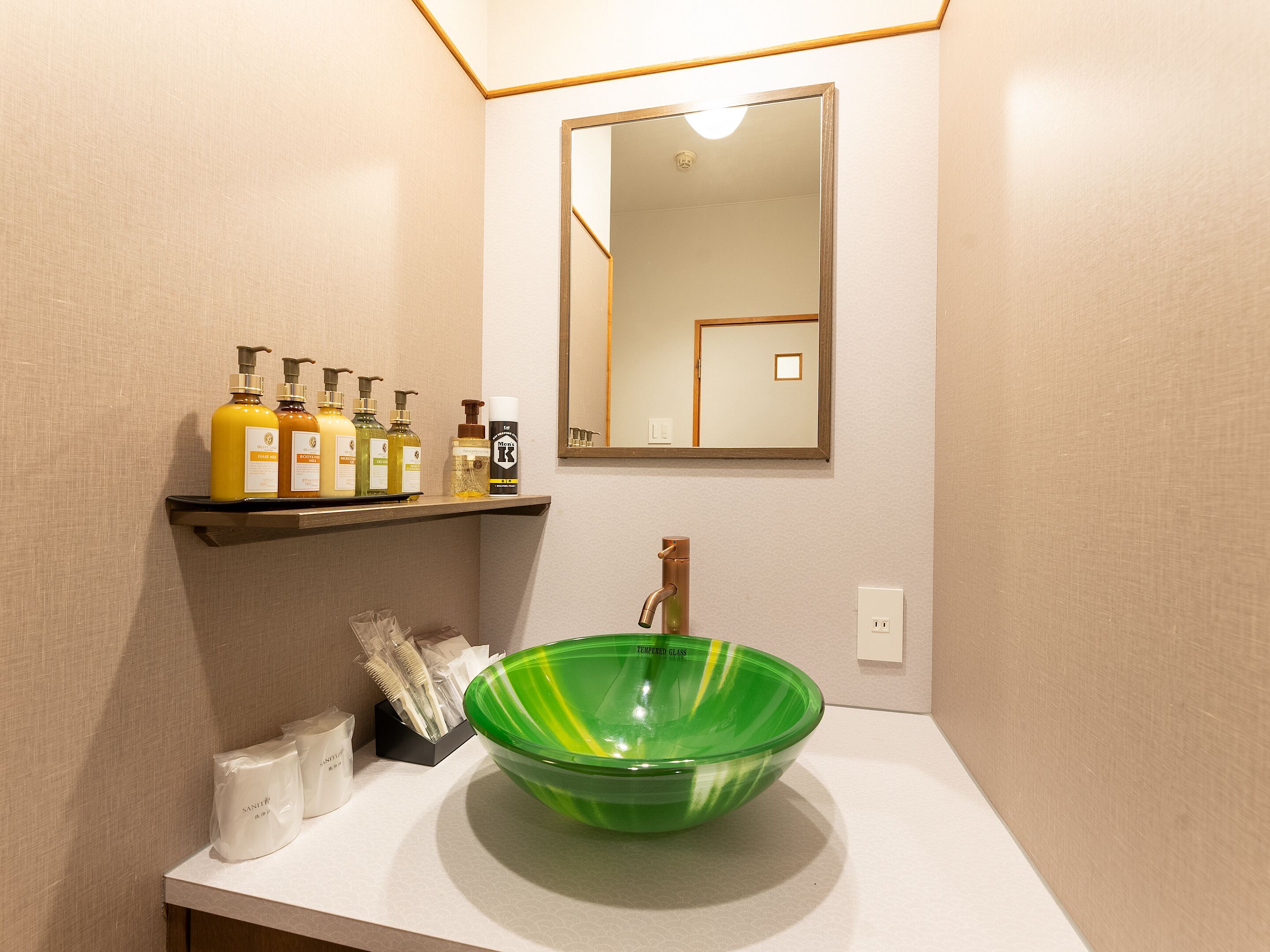 A bathroom with a green glass bowl sink, a mirror, and shelves with toiletries.