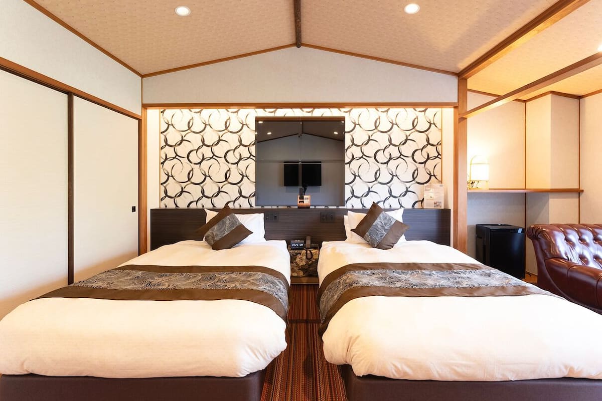 A hotel room with two beds, a TV, a desk, and a chair.