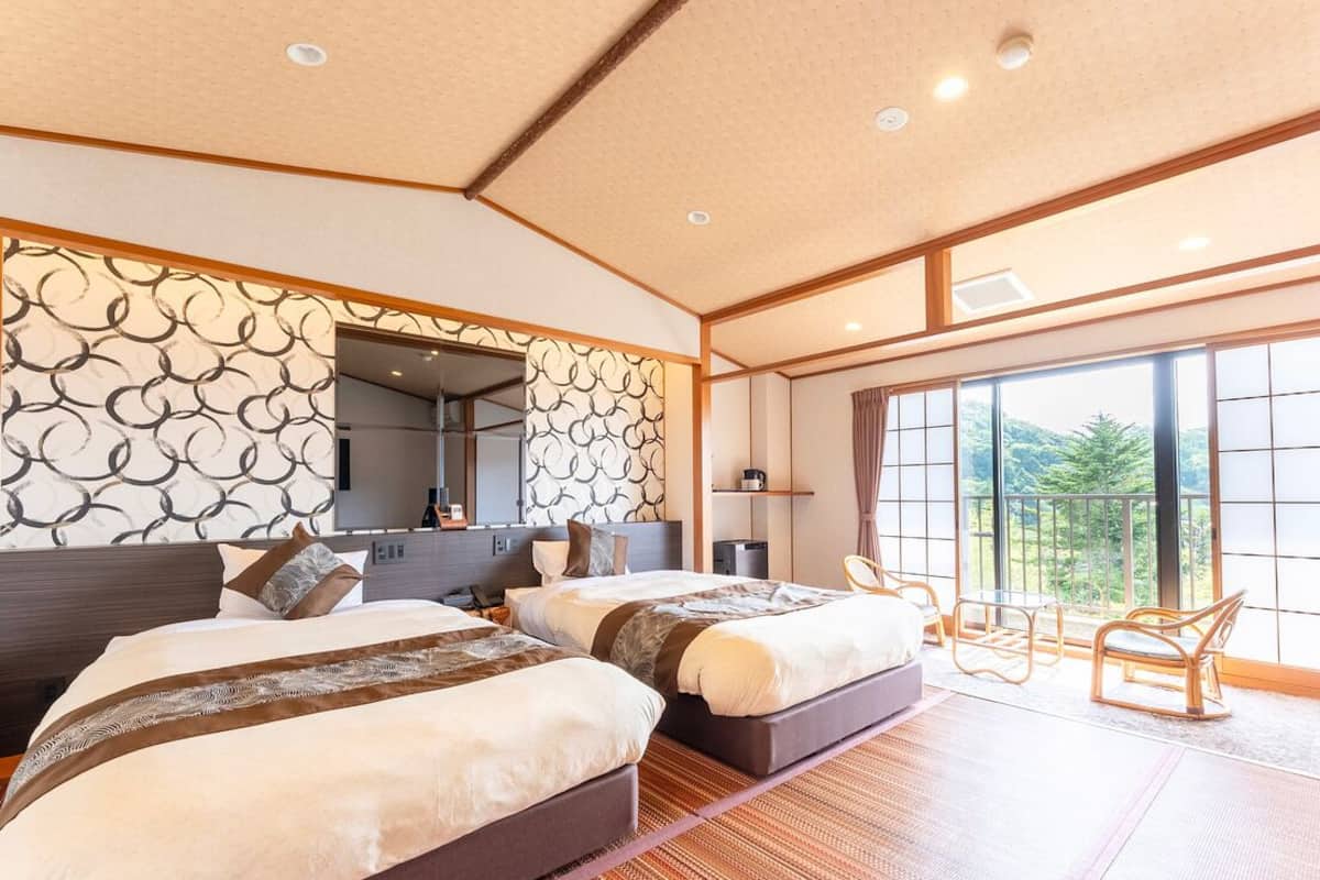 A hotel room with two beds, a large window, and a view of greenery.