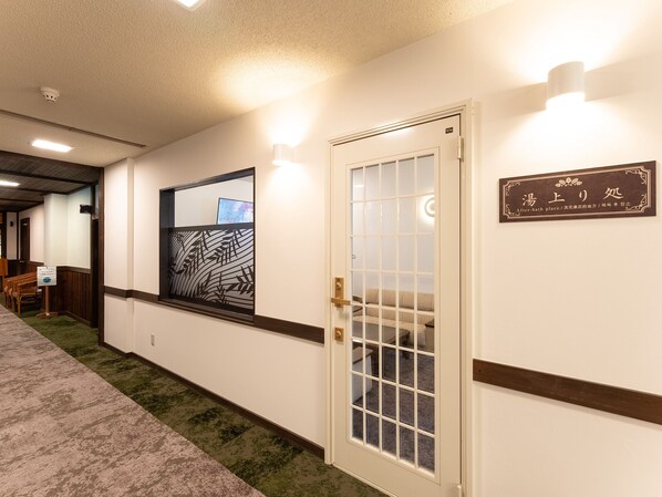 A hotel corridor with a reception area, a waiting area with chairs, a reception desk, and a sign indicating the after-bath place. - Livemax Resort Yuhigaura Kitu Onsen (Kyotango)