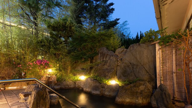 A serene outdoor hot spring area with a wooden deck, large rocks, and lush greenery. - Livemax Resort Yuhigaura Kitu Onsen (Kyotango)
