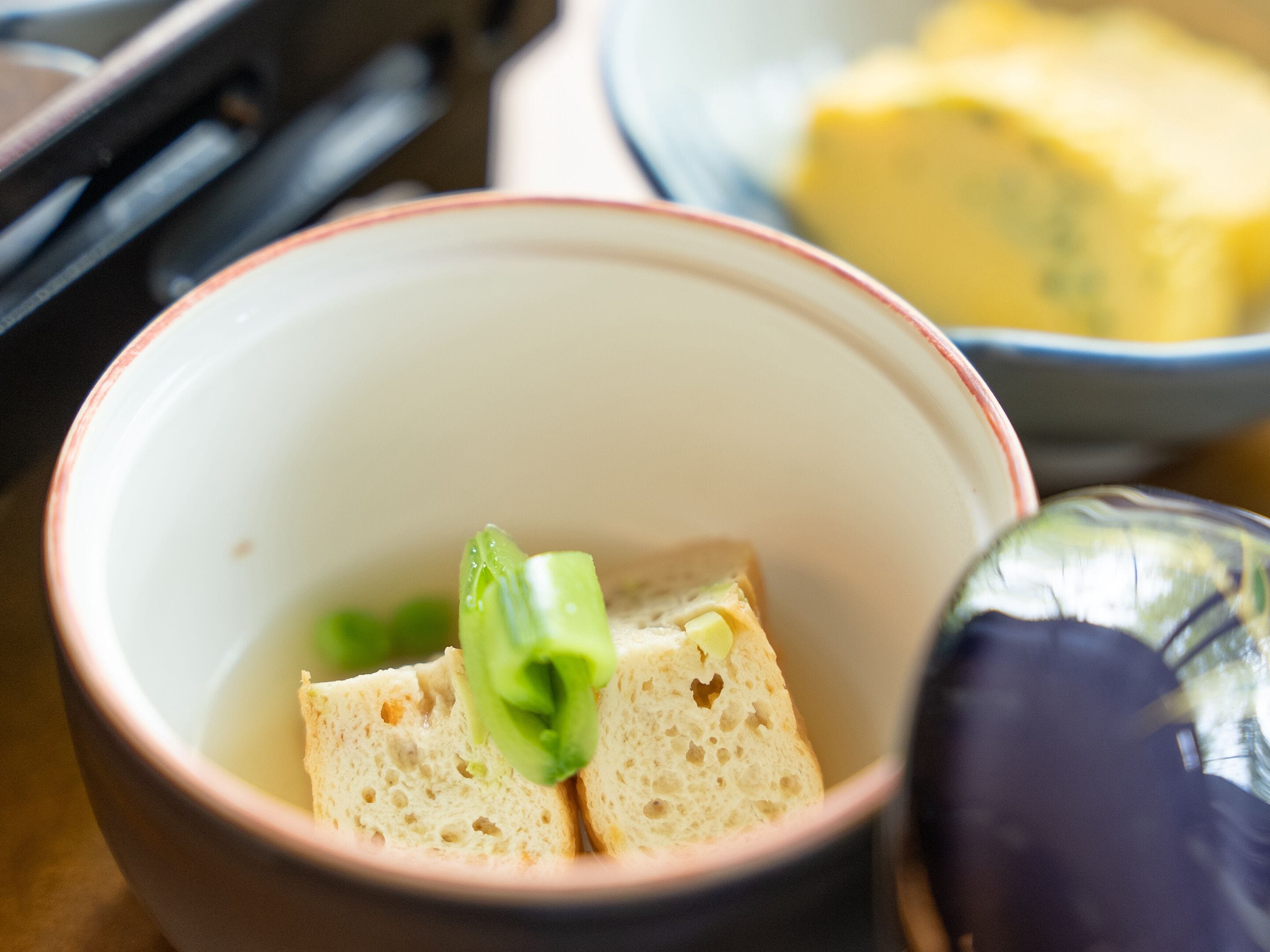 A bowl with two slices of bread and a green vegetable, possibly a cucumber, on a table.