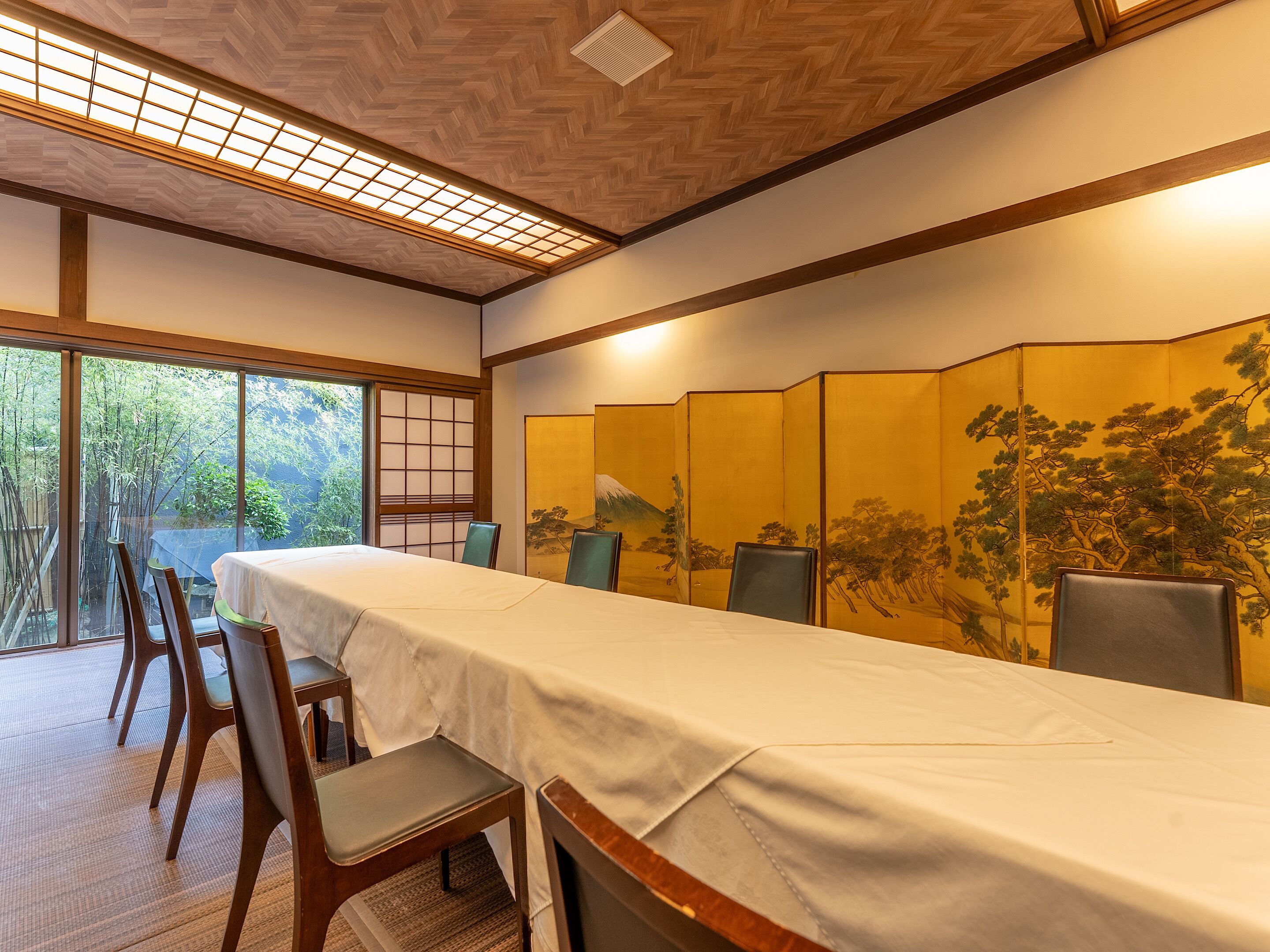 Habitació tradicional japonesa amb sòl de tatami, una taula baixa amb estovall i una porta corredissa amb una pintura de bosc.