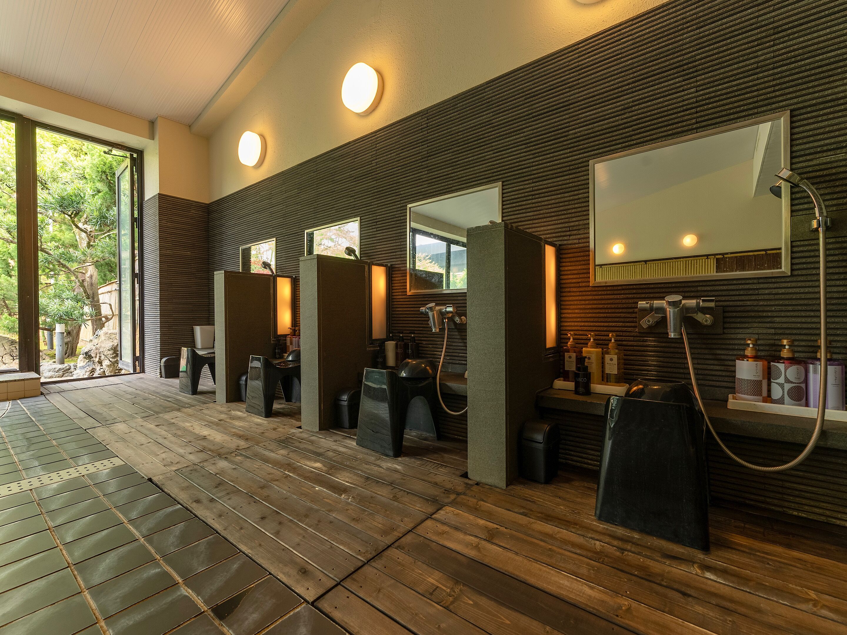 Un bagno moderno con pavimento in legno, lavabi singoli con specchi e un'ampia finestra che permette l'ingresso di luce naturale.