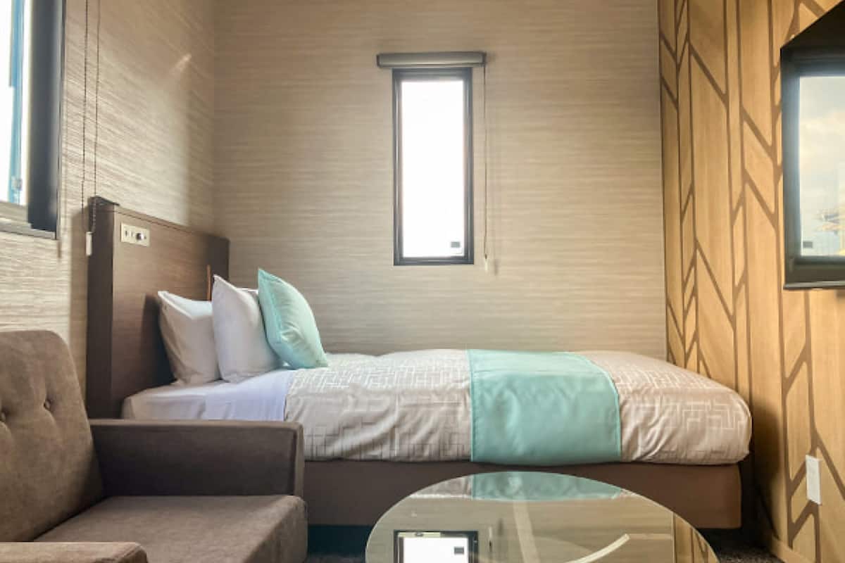 A hotel room with a bed, a chair, a small table, and a window.