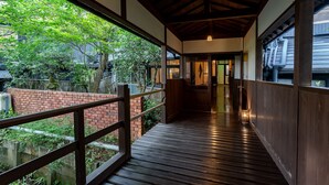 A covered wooden walkway with a brick wall on one side and a view of greenery and buildings on the other. - Livemax Resort Yuhigaura Kitu Onsen (Kyotango)