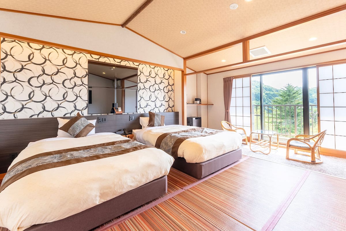 A modern hotel room with two beds, a large mirror, a desk, and a balcony with a view of the outdoors.