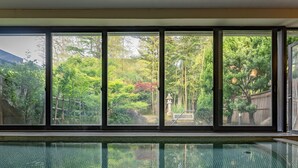 A swimming pool with a clear view of a lush garden through large windows. - Livemax Resort Yuhigaura Kitu Onsen (Kyotango)