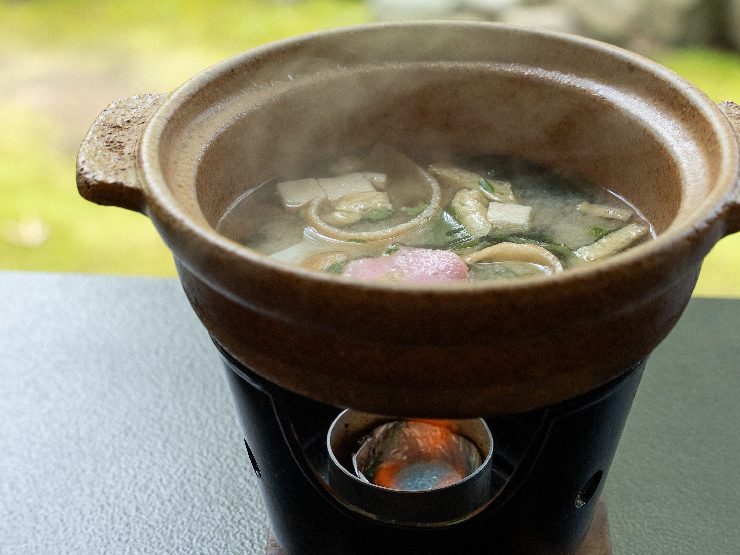Una olla de barro tradicional con tapa, colocada sobre una estufa con llamas visibles debajo.