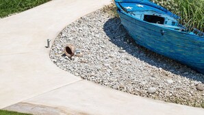 A pathway leading to a beach area with a blue boat, palm trees, and a white canopy structure. - White Pearls Luxury Suites - Adults Only (Kos)