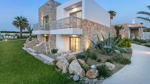 A modern two-story house with a stone facade, a balcony with a railing, and a well-maintained garden with rocks and plants. - White Pearls Luxury Suites - Adults Only (Kos)