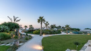 A well-maintained garden with a curved pathway, palm trees, and various plants. - White Pearls Luxury Suites - Adults Only (Kos)