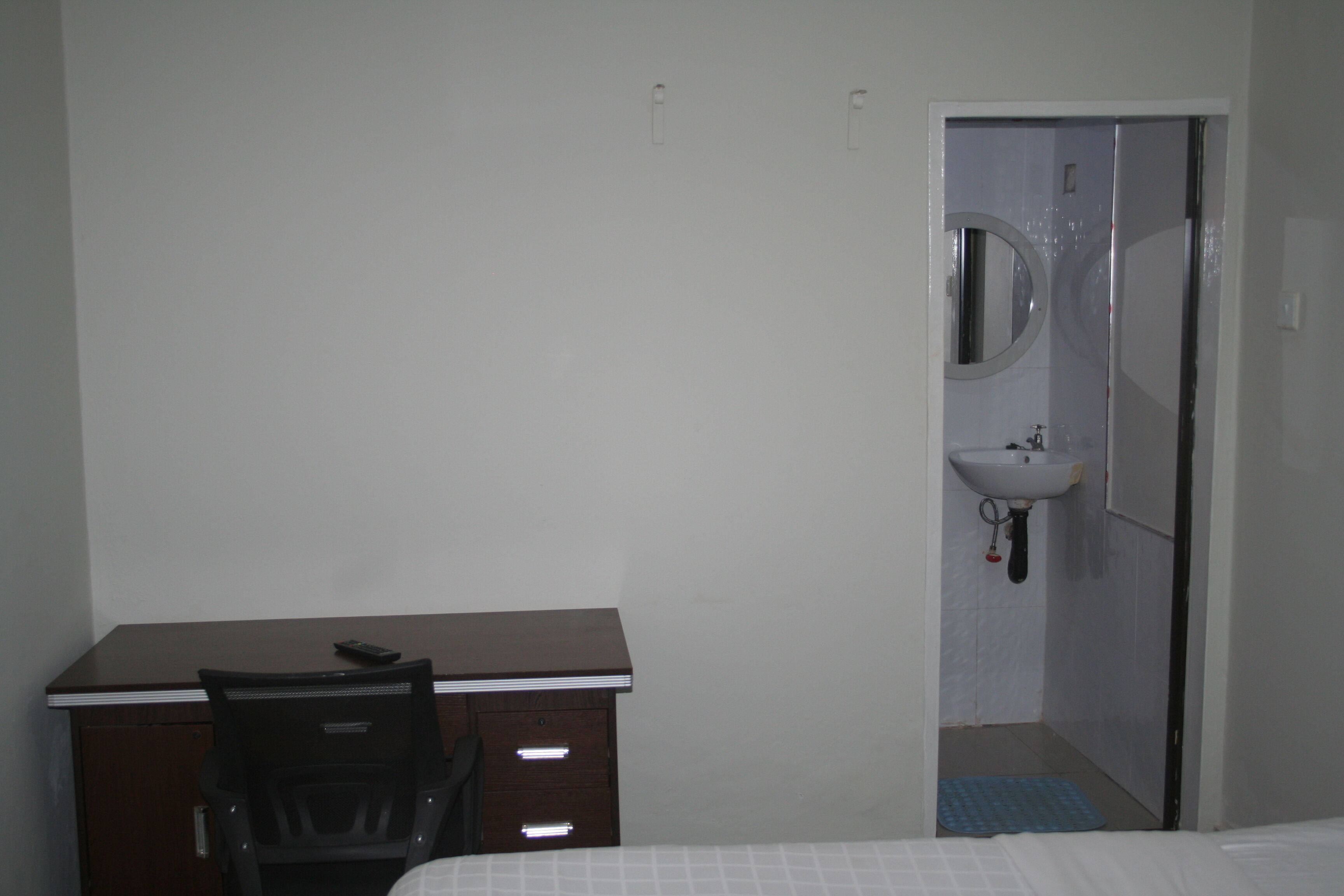 A hotel room with a bed, a desk with a chair, a small bathroom with a sink and mirror.