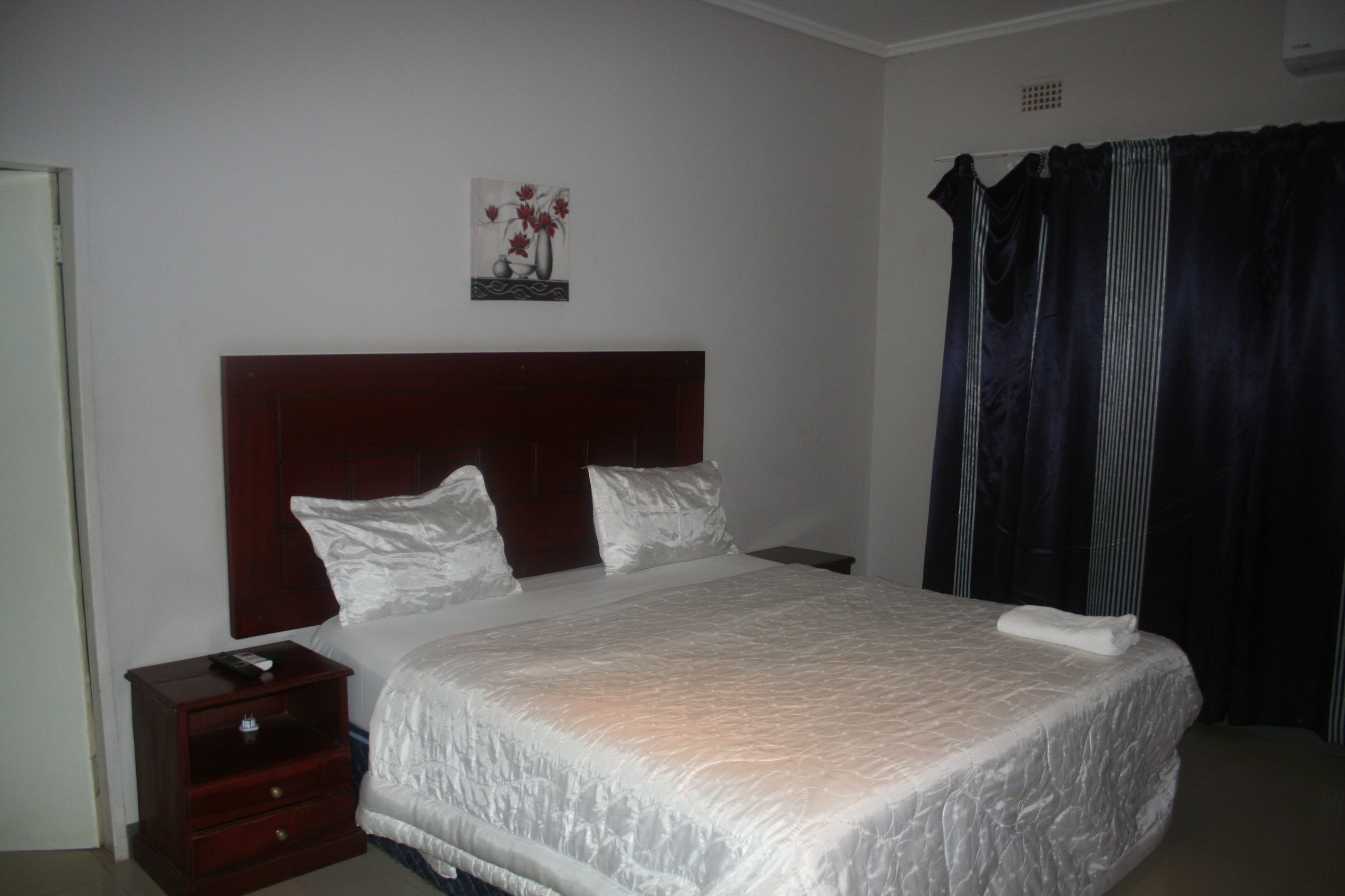 Una cama bien hecha con ropa blanca, un cabecero de madera y una mesita de noche con un control remoto.