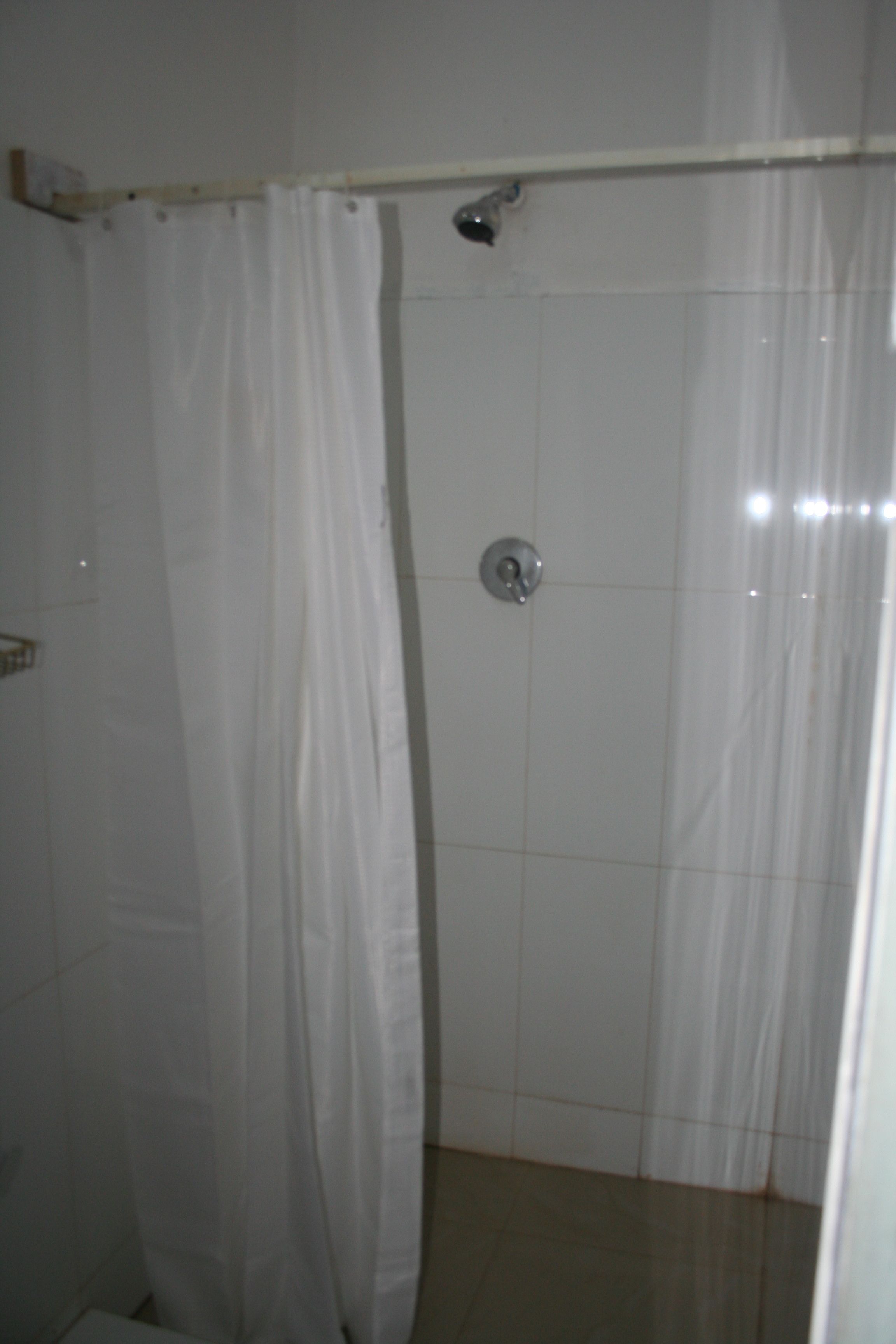 A small, enclosed shower area with a white curtain and a showerhead mounted on the wall.