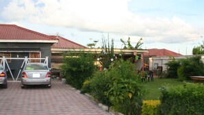 A paved driveway leading to a house with a red roof, surrounded by greenery and a parked car. - Honeybed Lodge (Lusaka)