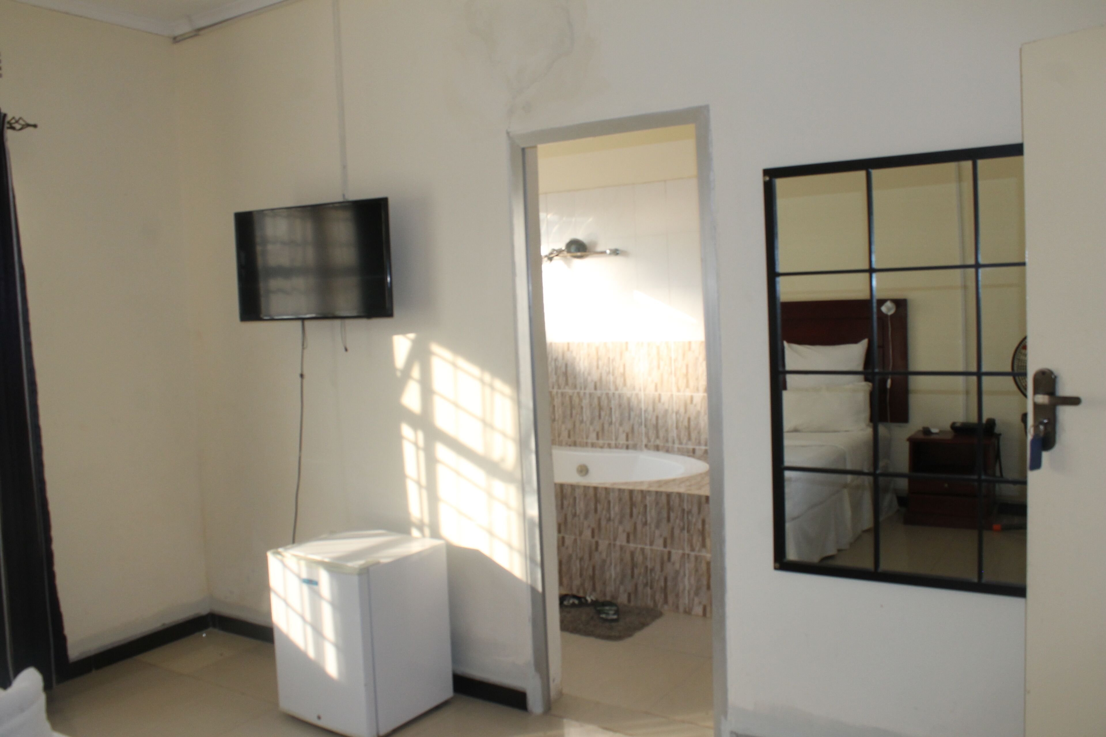 A small, compact room with a bed, a television mounted on the wall, a sink, and a mirror.