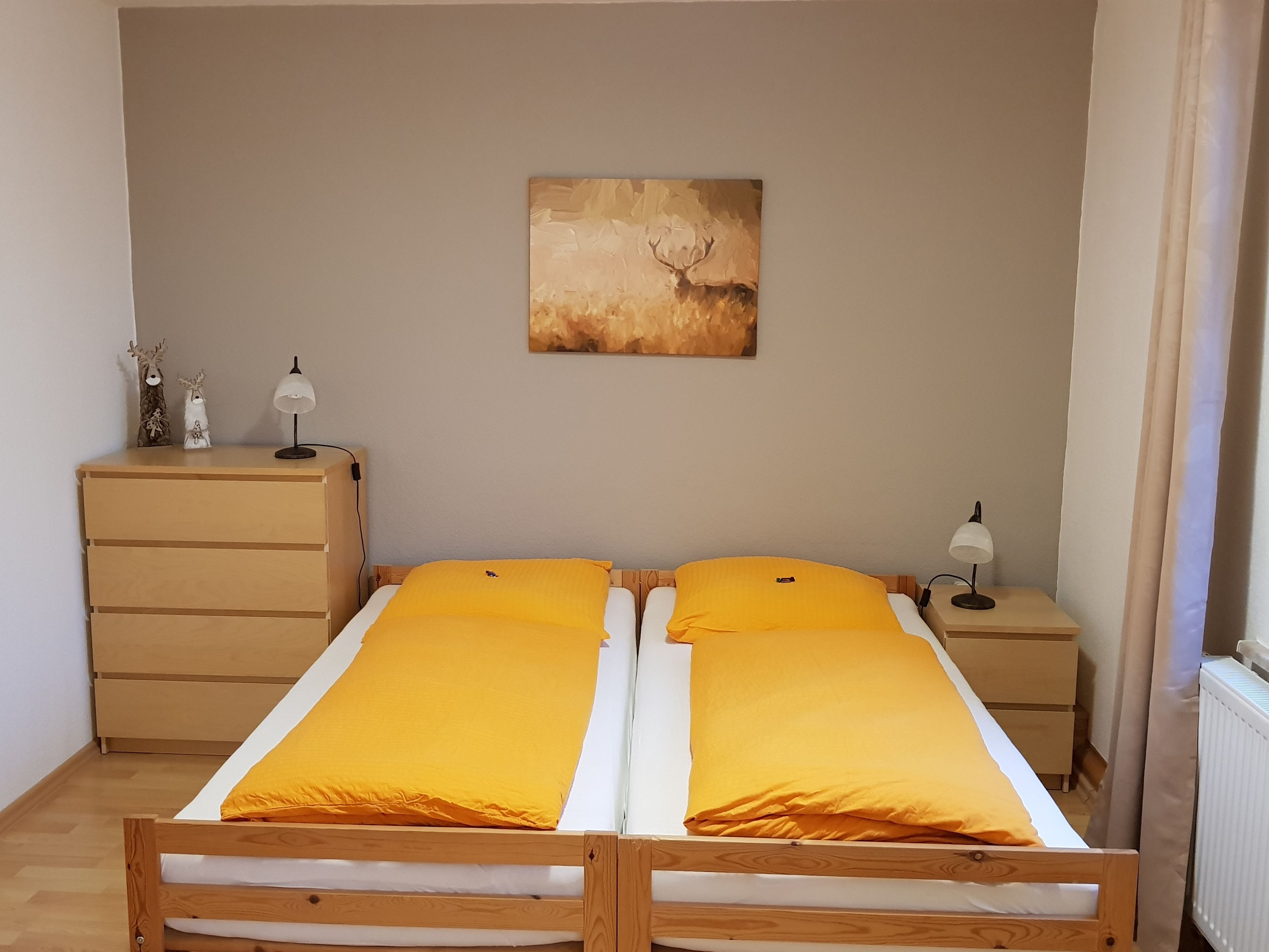 A bedroom with a double bed, a nightstand with a lamp, a dresser, and a painting on the wall.
