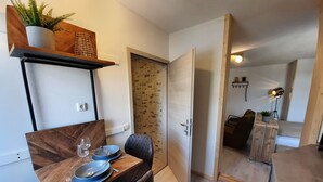 Ett kompakt bostadsutrymme med en matplats som har ett träbord och en vadderad stol. Ett litet pentry syns i bakgrunden.
