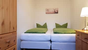 A bedroom with two single beds, a wooden wardrobe, a bedside table with a lamp, and a painting on the wall.