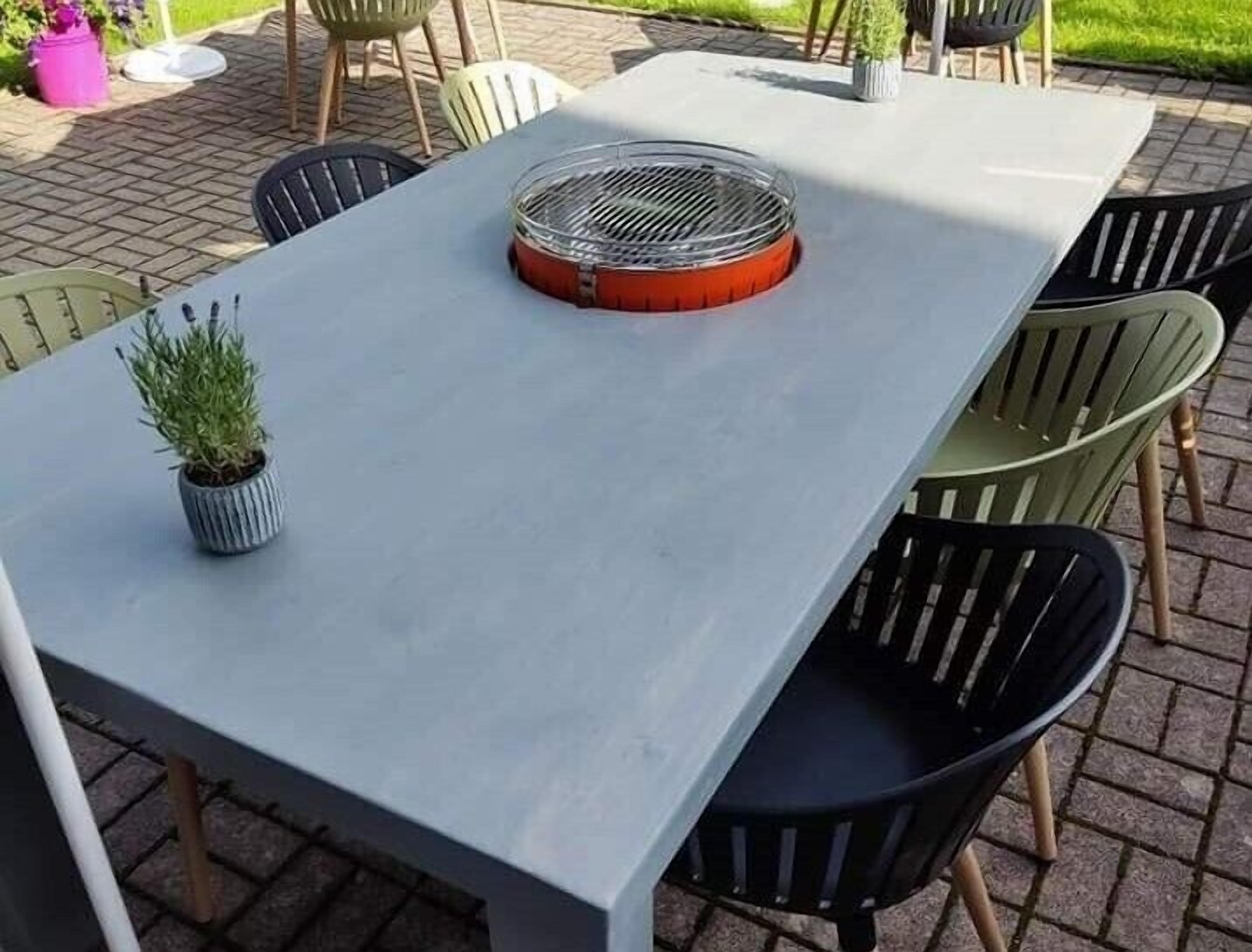 A rectangular outdoor table with a grill on top, surrounded by chairs.