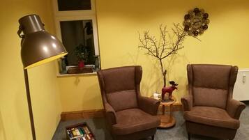 A room with two brown armchairs, a floor lamp, a small table with a moose figurine, a decorative tree, and a window with a view of the outside.