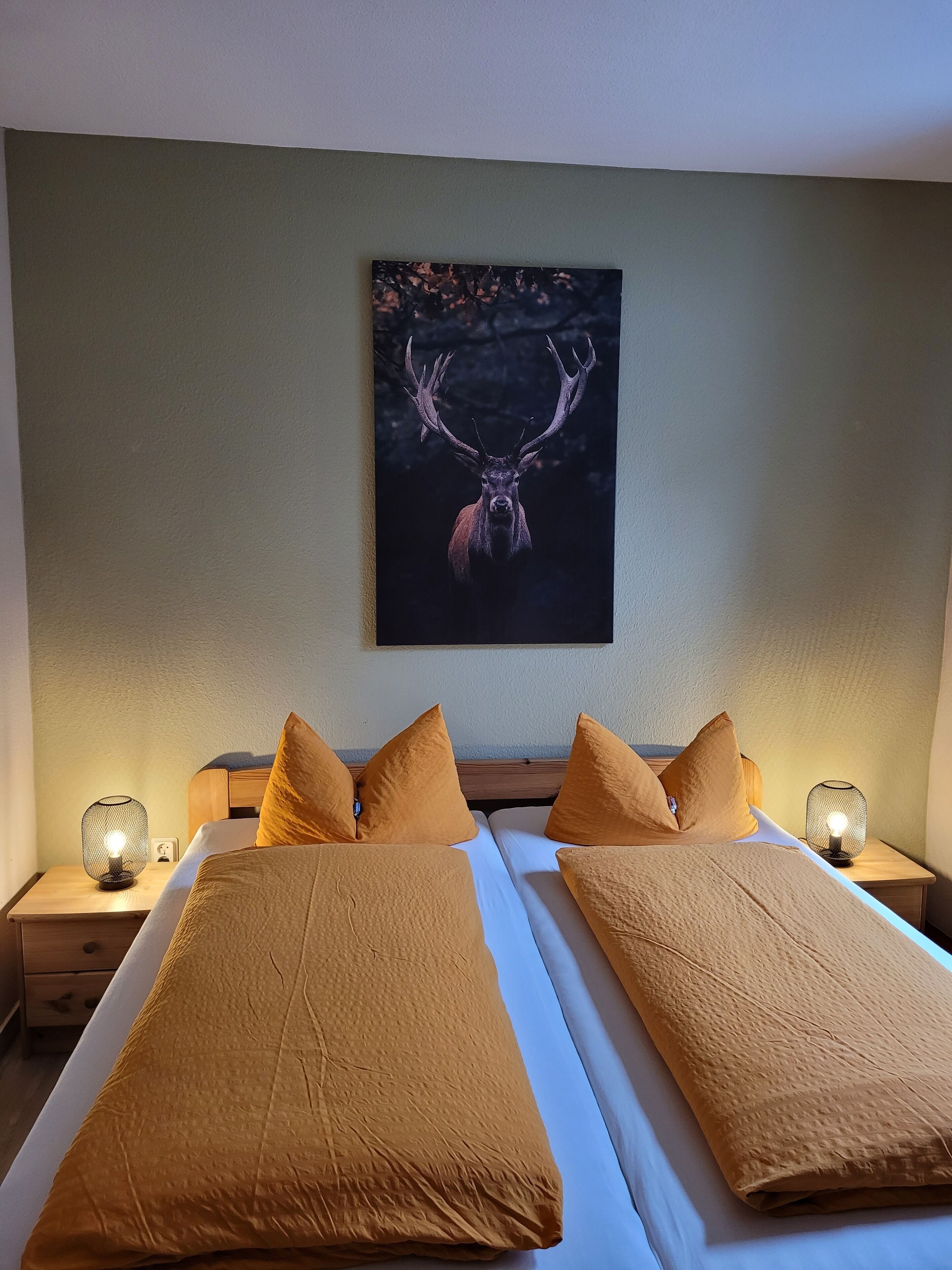 Een hotelkamer met twee bedden, een groot kunstwerk van een hertenhoofd aan de muur en twee bedlampjes.