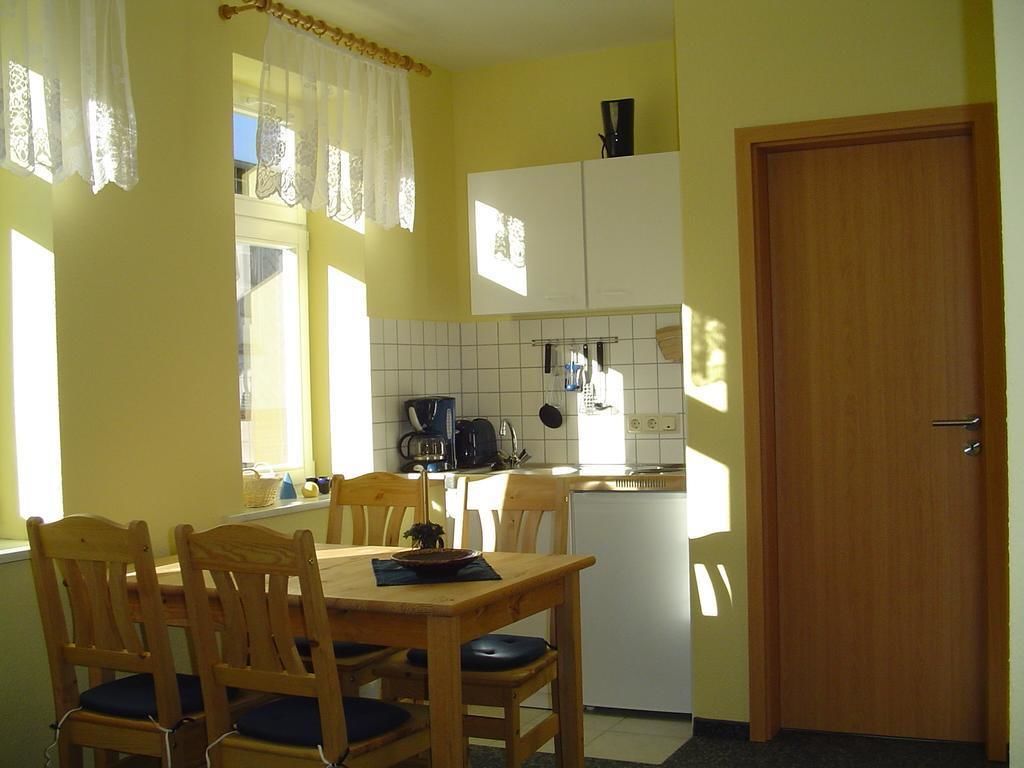 A compact kitchen with a dining area, featuring a wooden table and chairs, a refrigerator, and a coffee maker.