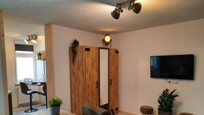 Ett modernt vardagsrum med ett matbord i trä, bekväma sittplatser, en stor spegel och en platt-TV som är monterad på väggen.