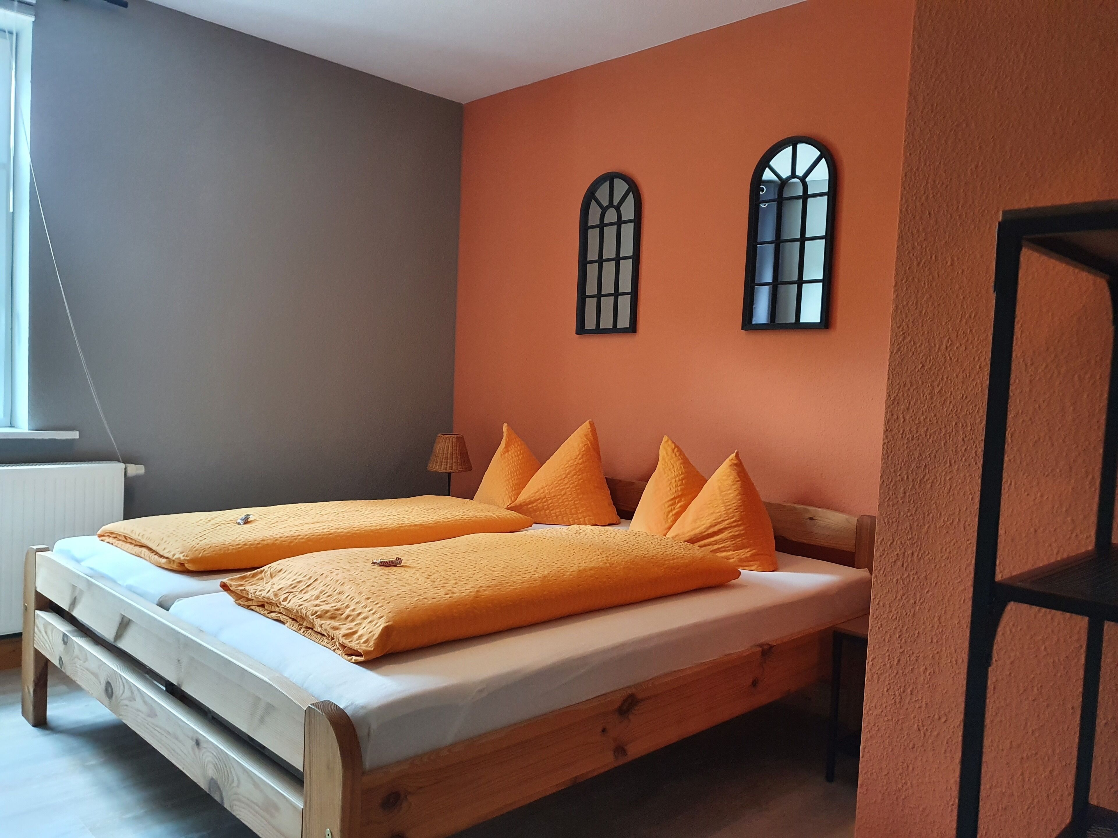 A bedroom with a wooden bed, orange bedding, and two arched windows on the wall.