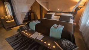 A well-appointed bedroom with a canopy bed, a bedside table with candles, and a zebra-patterned rug. - Track and Trail River Camp (South Luangwa National Park)