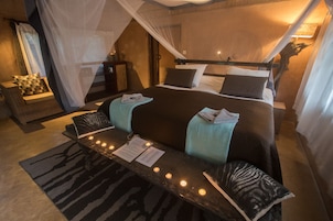 Quarto bem decorado com uma cama a céu aberto, mesa de cabeceira com velas e um tapete com padrão de zebra.