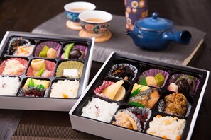 Duas lancheiras japonesas com diversos alimentos, uma chaleira e duas xícaras sobre uma mesa.