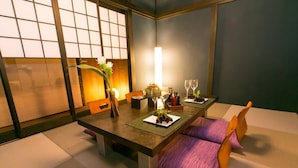 A dining area with a low table, cushioned seating, and a vase with flowers. - Hosta Nijo Aoi (Kyoto)