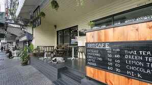 An outdoor seating area with a wooden table and chairs, a blackboard menu, and hanging plants. - 1989 Sukhumvit Bangkok - Hostel (Bangkok)