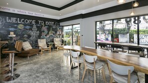 A modern cafe with a mural, wooden furniture, and large windows. - 1989 Sukhumvit Bangkok - Hostel (Bangkok)