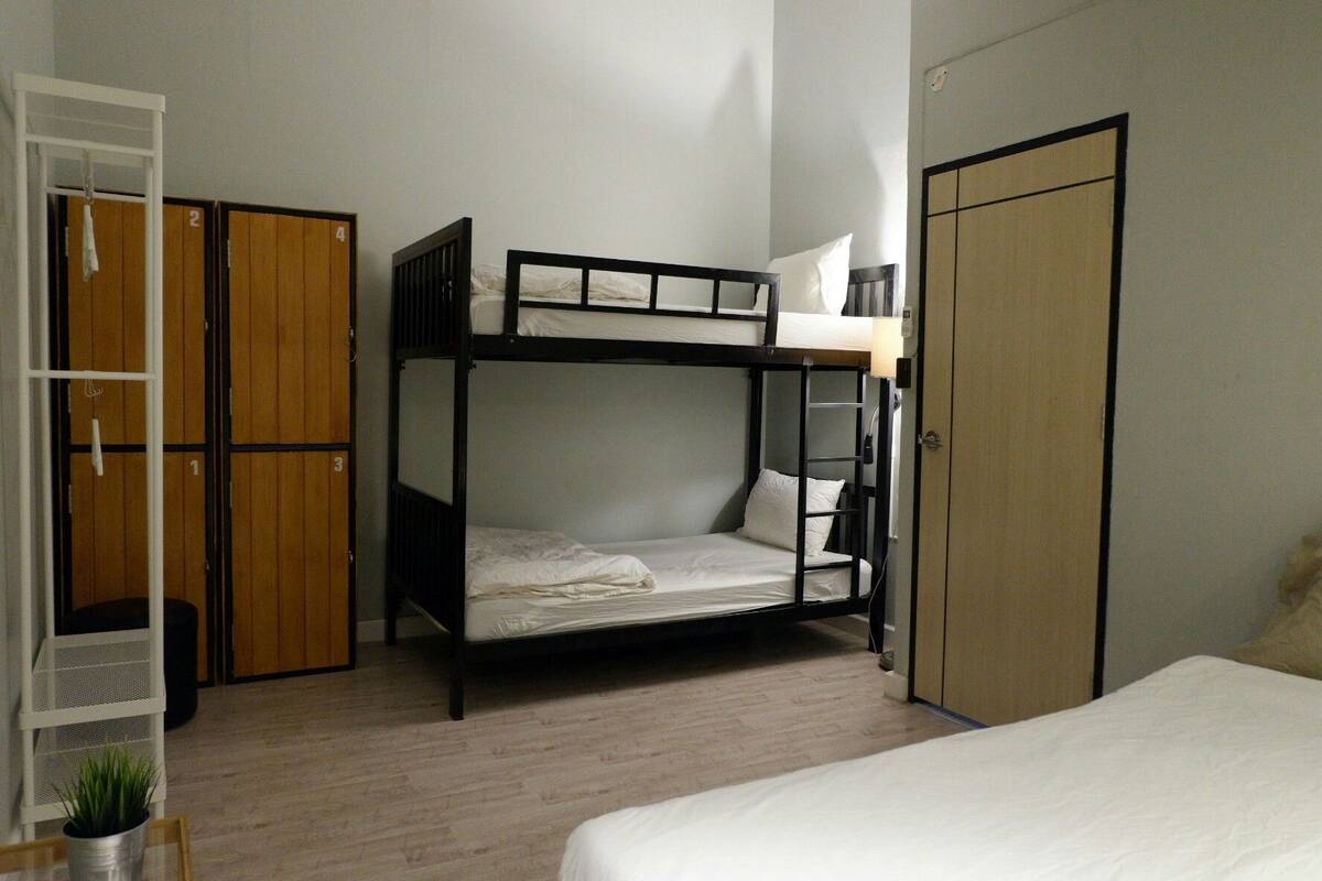 Habitación con literas, un armario, una pequeña mesa con una planta y una puerta.