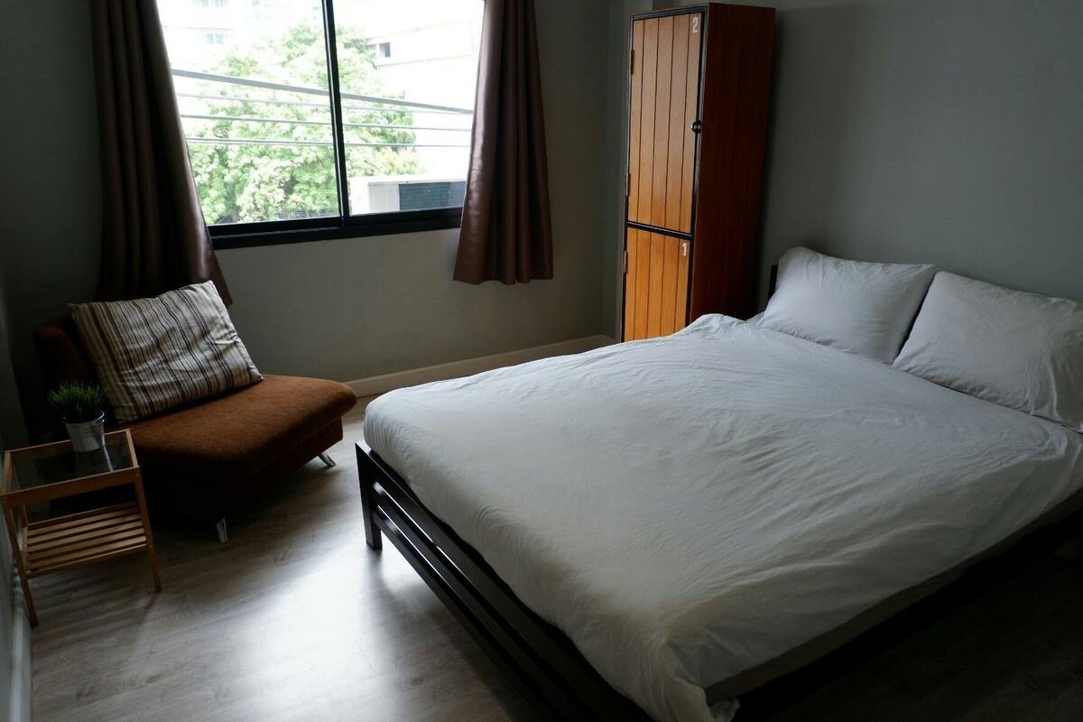Un dormitorio con cama, una silla, una mesita con una planta y un armario.