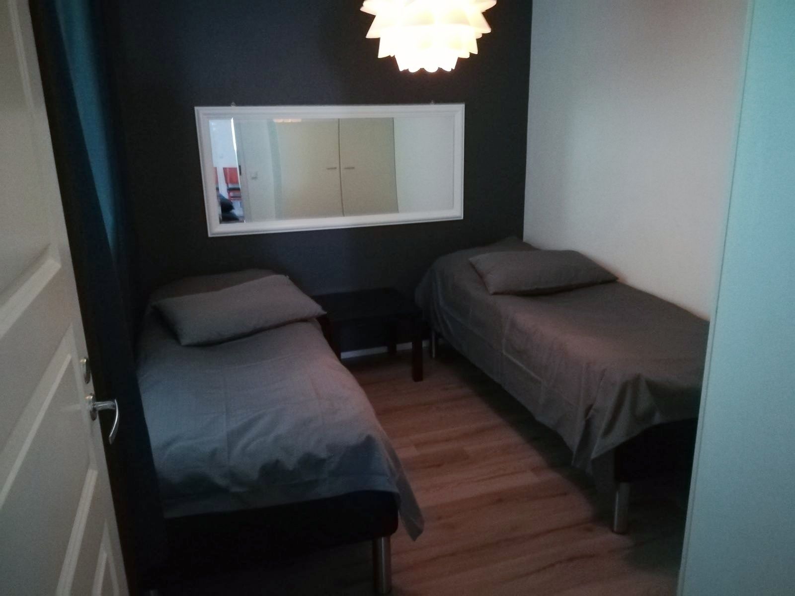 Une petite pièce faiblement éclairée, avec deux lits simples, un miroir et un plancher en bois.