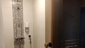 A small, tiled shower room with a wooden ceiling and a door leading to a dark room. - Hostel Racuna (Kokkola)
