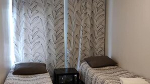 A small, compact room with two single beds, a small table, and a window with leaf-patterned curtains. - Hostel Racuna (Kokkola)