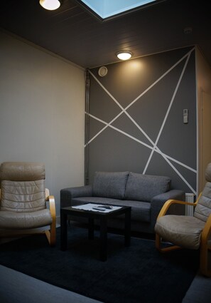 A modern room with a grey sofa, two leather chairs, a small table, and a geometric wall design.