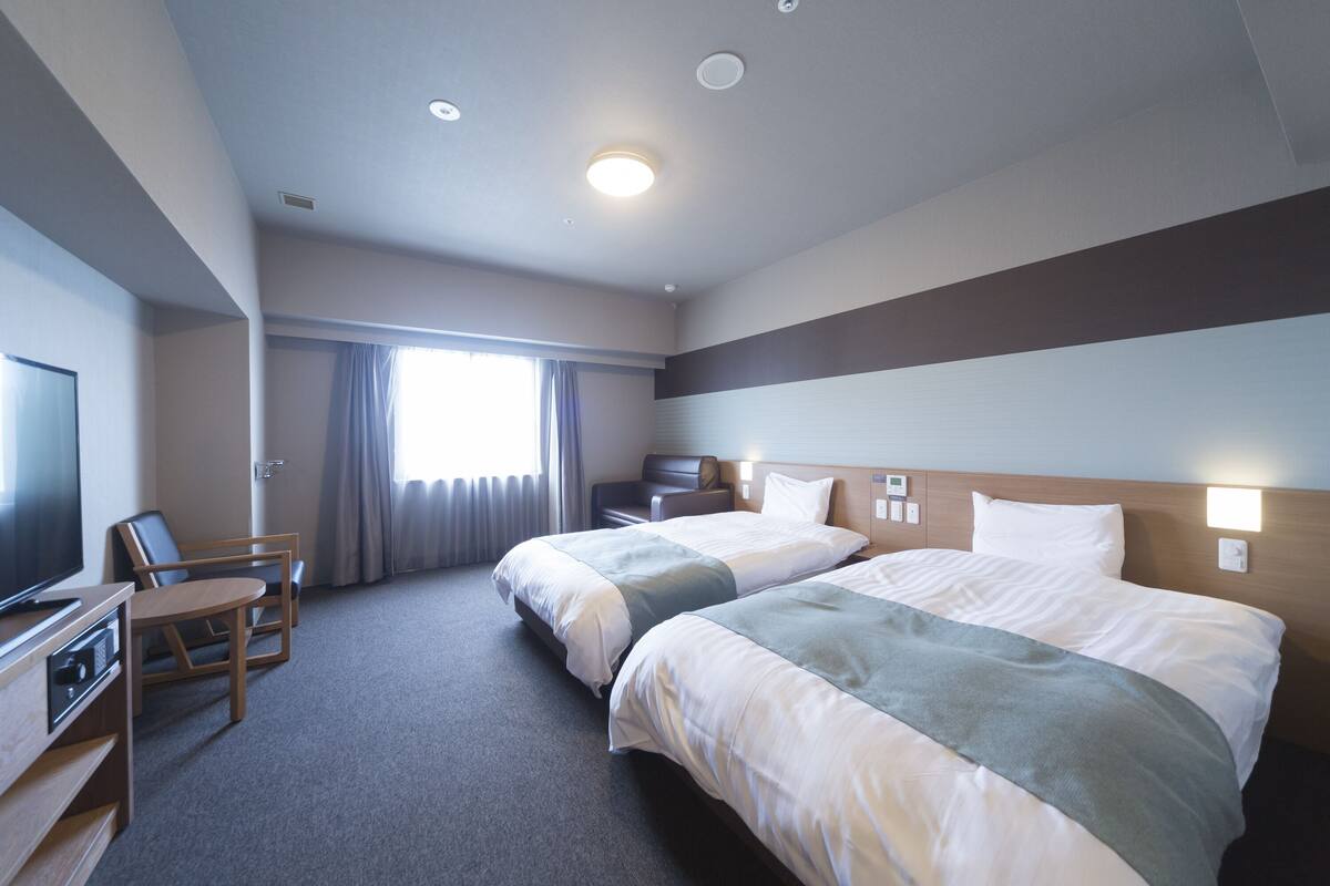 A hotel room with two beds, a desk with a chair, a television, and a window with curtains.