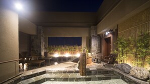 An outdoor pool area with stone flooring, seating, and a stone pillar.